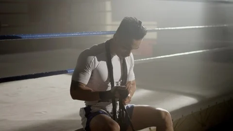 Muay Thai fighter wraps hands while sitting on the edge of a boxing ring 스톡 동영상 104556809