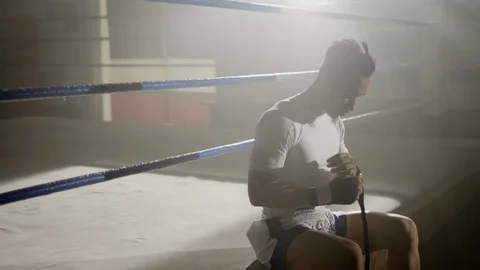 Muay Thai fighter wraps hands while sitting on the edge of a boxing ring Stock Footage 104559104