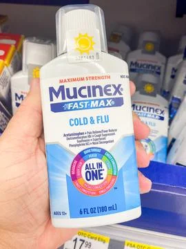 Mucinex Fast-Max maximum strength cold and flu liquid medicine bottle held .. Stock Photos