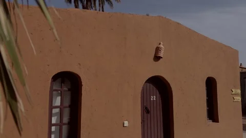 Mud brick Moroccan building with arched wooden doors palm fronds and wall Stock Footage 336001443