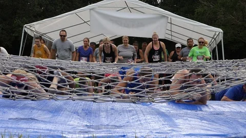 Mud Run Participants crawling under a cargo net slip and slide obstacle. Stock Footage 114748140