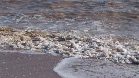 Muddy brown waves with white sea foam beat against the sandy shore Stock Footage 221162549