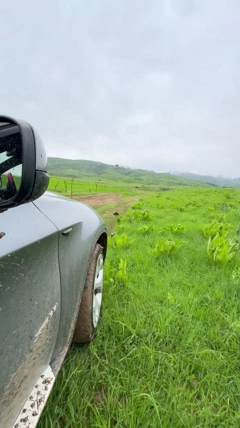 A muddy car driving through a lush green countryside with hills in the Stock Footage 276427736