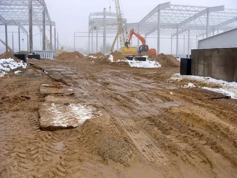 Muddy construction area with structural steel and cranes, work in progress. Stock Photos