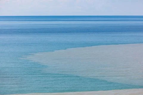 Muddy river current blends with blue sea water 스톡 사진