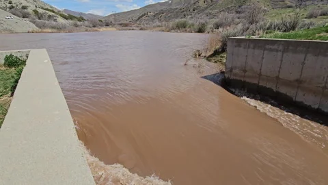Muddy runoff water from mid-stream catch pond overflows into spillway Stock Footage 240503182