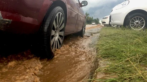 Muddy water flowing down stream against a parked car and tire Видео 102714966