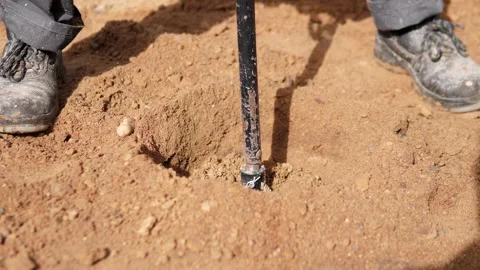 Muddy work boots standing beside digging tool on reddish soil, with disturbed Vidéo 344910798