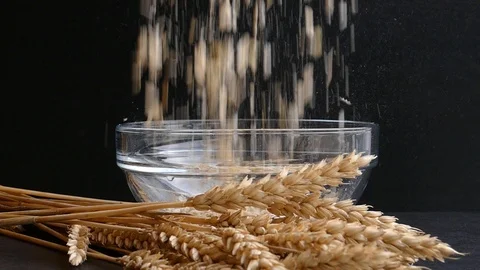 Muesli falling into empty transparent glass bowl,pour in milk and ears of wheat Stock Footage 97711058