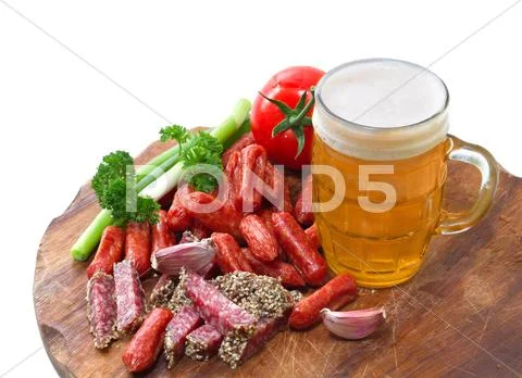Mug of beer and an assortment of salami and vegetables on a cutting board Stock Photos