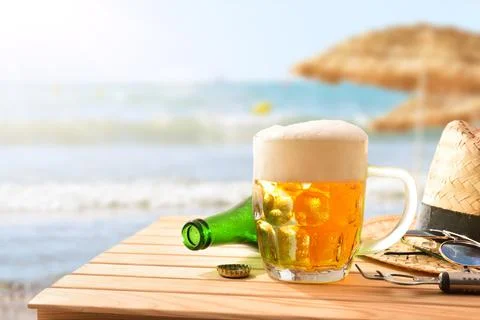 Mug of beer on table on beach with straw umbrellas Stock Photos