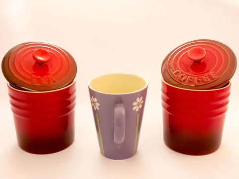 A mug in between a red jar of tea and a red jar of coffee Stockfoto's