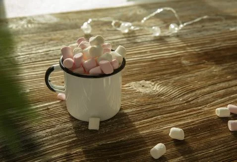 Mug of cocoa with marshmallows on a wooden table and garland. Stock Photos