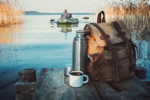 Mug of coffee or tea, backpack of traveller and thermos on pier. Stock Photos