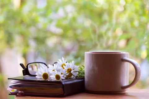 Mug, daisies, Notepad, glasses. The concept of a Sunny summer morning. Stock Photos