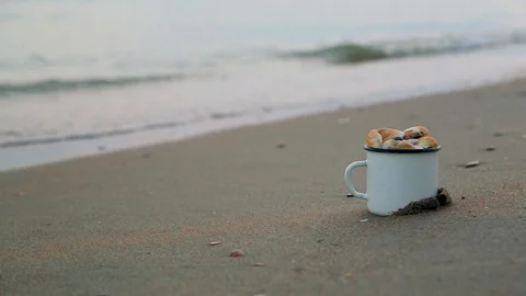 Mug filled with shells standing on shore against male legs running along shore Stock Footage 93110726