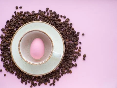 Mug full of easter egg on plate surrounded by coffee beans on pink background Stock Photos