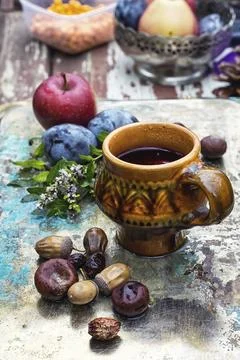 Mug with herbal tea on background of apples and plums in the autumn garden Stock Photos