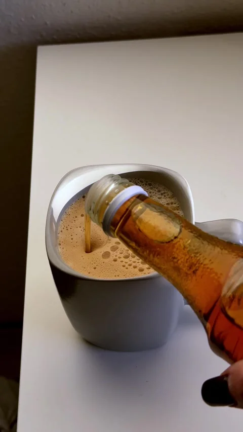 Mug holding warm brown beverage receiving golden liquid stream from clear bottle 스톡 동영상 333181099