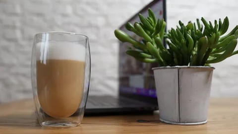 A mug of hot cappuccino stands on a table with a laptop Stock Footage 221653295