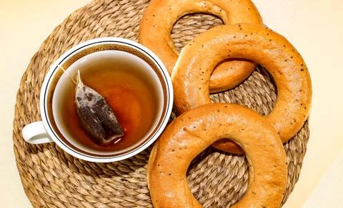 A mug of tea is on the table and next to it are ruddy bagels with poppy seeds 스톡 사진