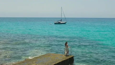 Mujer al final de un embarcadero mirando al mar con un velero de fondo 動画素材 158236811
