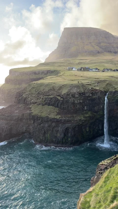 Múlafossur waterfall dropping into the Atlantic Ocean with Gásadalur village in  Video stock 335269457