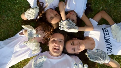 Multi aged volunteers laying on grass and waving into camera Stock Footage