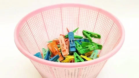 Multi color plastic laundry clips falling into a basket on the white background Video stock 306445595