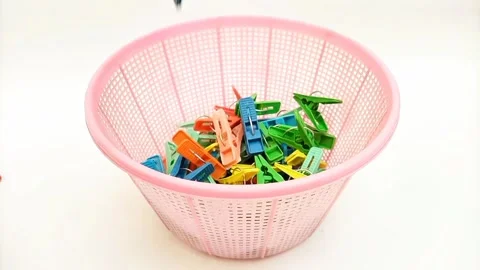 Multi color plastic laundry clips falling into a basket on the white background Video stock 306445596