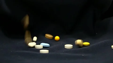Multi-colored and varied pills spill out on a black background close-up Stock Footage 337426848