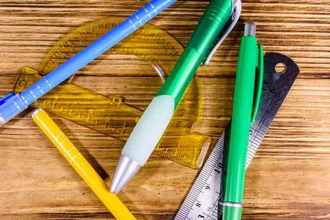 Multi colored ball pens, protractor and ruler on a wooden table. Top view Stock Photos