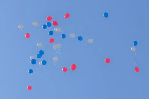 Multi colored balloons fly away into the clear blue sky on a sunny day Stock Photos