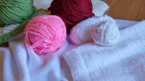 Multi-colored balls of green, red, pink and white yarn lying next to a white Fotos de archivo