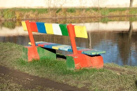 Multi-colored bench standing in a park near the pond Stock Photos