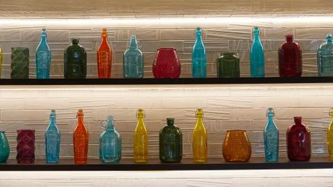 Multi-colored bottles of different shapes stand in a row on the shelves Stock Photos