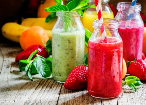 Multi-colored bottles with fresh fruit smoothies with striped straws, berries Stock Photos