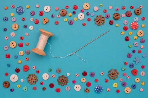 Multi-colored buttons are scattered on the table, a needle, a spool of thread Stock Photos