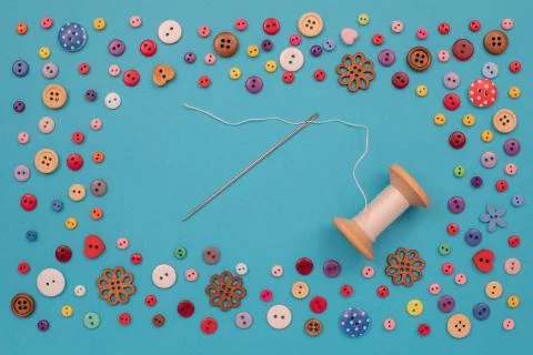 Multi-colored buttons are scattered on the table, a needle, a spool of thread Stock Photos