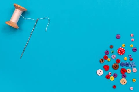 Multi-colored buttons are scattered on the table, a needle, a spool of thread Stock Photos