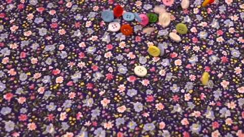 Multi-colored  buttons fall on a cotton navy fabric with a small floral pattern Stock Footage 317493265