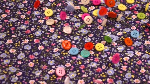 Multi-colored  buttons fall on a cotton navy fabric with a small floral pattern Stock Footage 317493300