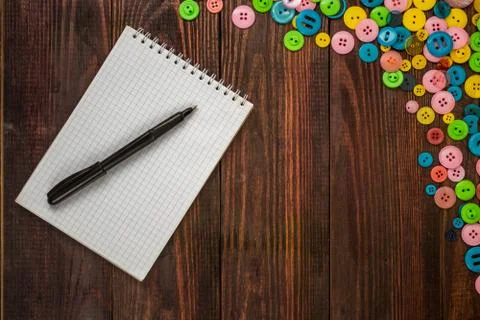 Multi-colored buttons of various sizes are scattered in the corner of a wooden Stock Photos