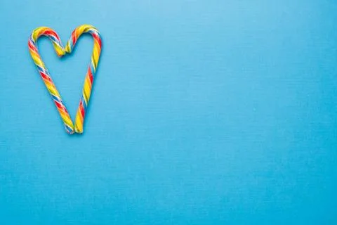 Multi-colored candy canes in the form of a heart on a blue background, copy Stock Photos