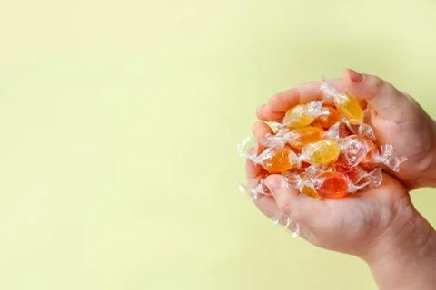 Multi-colored candy caramel in the hands of a child on a light yellow backgro 스톡 사진