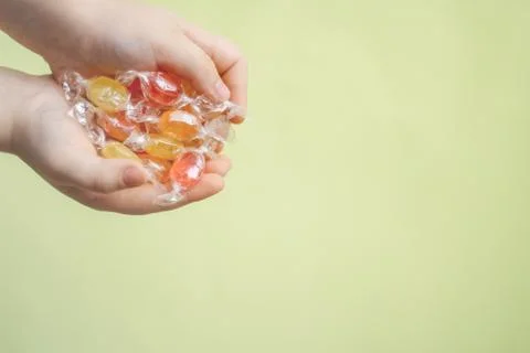 Multi-colored candy caramel in the hands of a child on a light yellow backgro Stock Photos