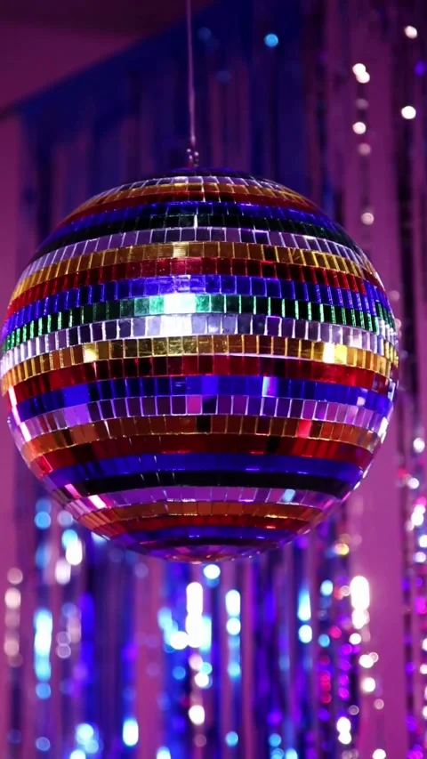 Multi colored disco ball spinning against purple tinsel background Video stock 331771949