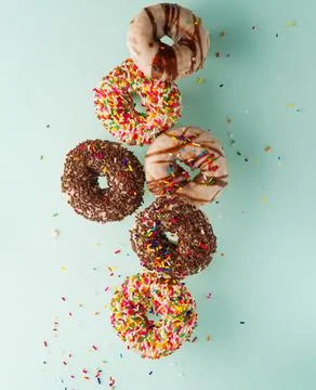 Multi-colored donuts covered with chocolate and sugar icing on a light blue b Stock Photos