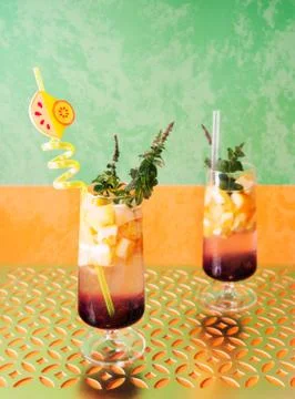 Multi-colored drinks with pieces of fruit, mint and an unusual straw. Stock Photos