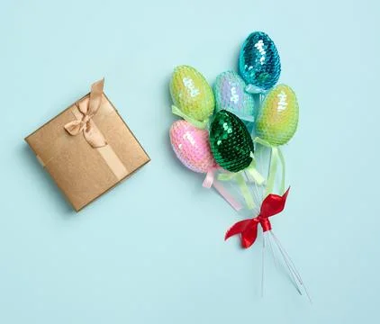 Multi-colored Easter decorative eggs in sequins and a gift on a blue backgrou Stock Photos